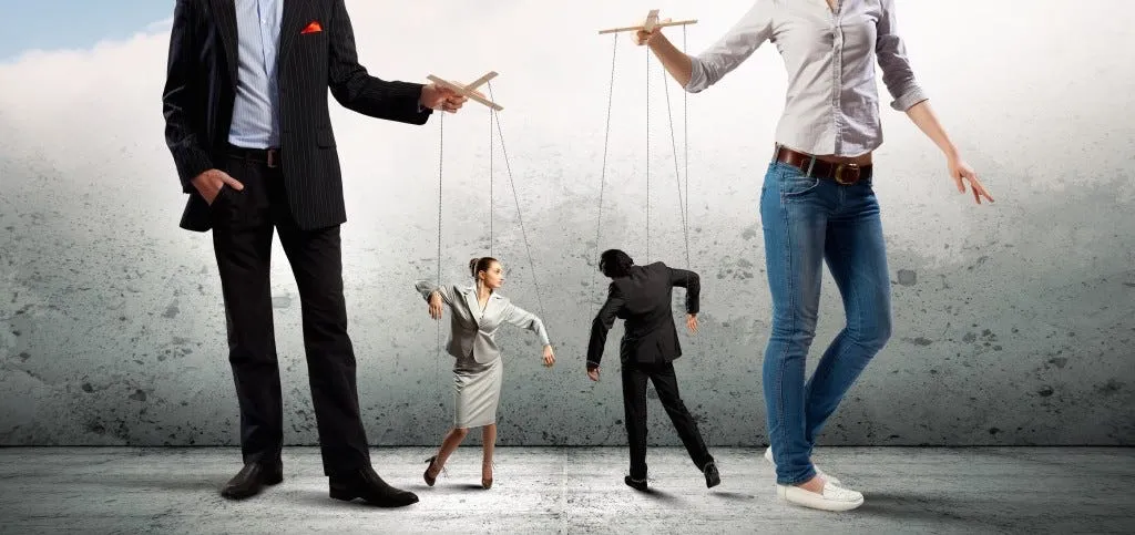 Duas figuras gigantes manipulam, como marionetes presas por fios, dois profissionais de terno