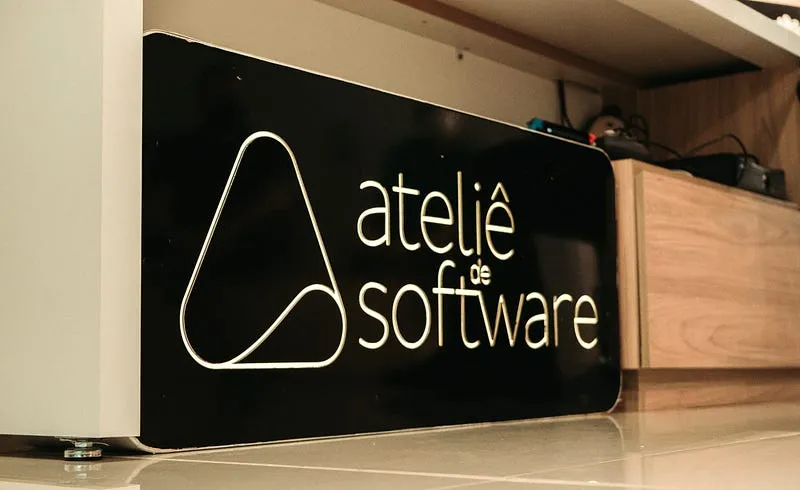 Letreiro preto com o logotipo do Ateliê de Software, um triângulo de cantos arredondados, apoiado sobre um balcão