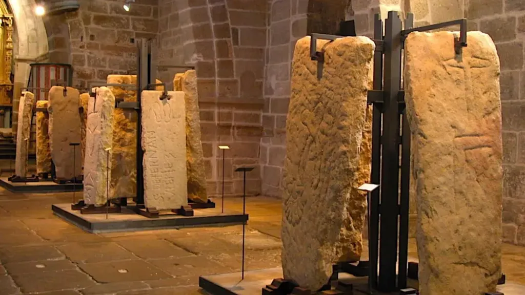 Lápides medievais de pedra, com sinais gravados, expostas em suportes de metal no interior da igreja de Santa María A Nova, em Noia