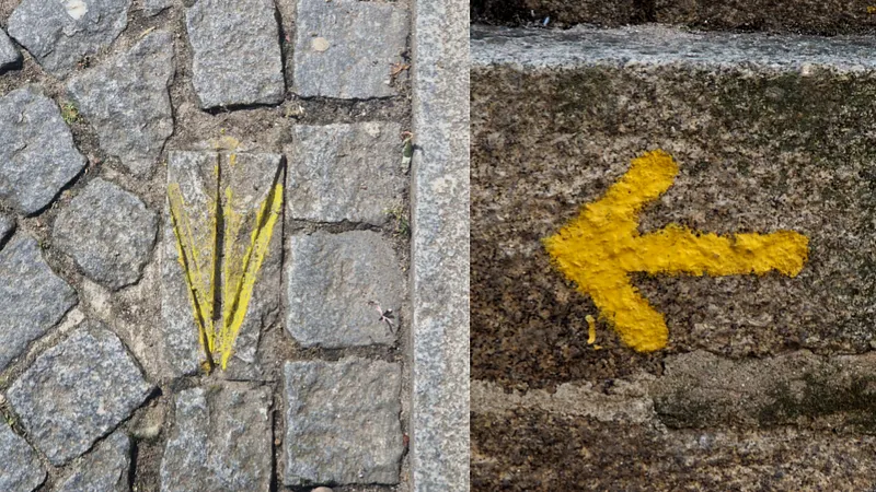 Uma concha estilizada pintada de amarelo no calçamento e uma seta amarela pintada numa pedra