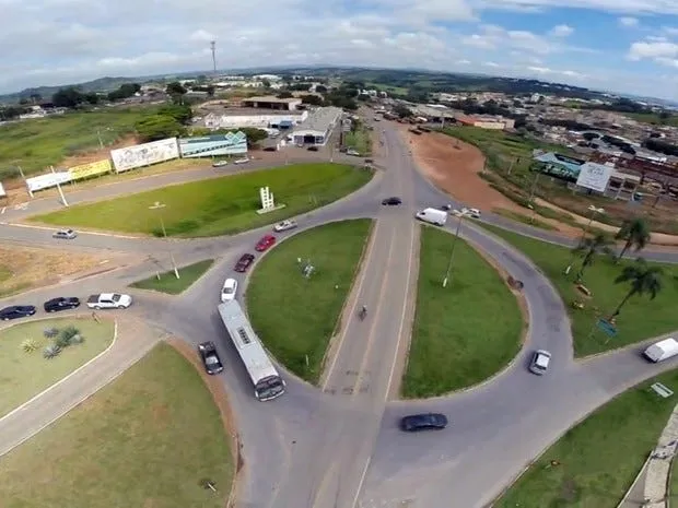Vista aérea de um trevo em nível em Alfenas, com carros, um ônibus e uma moto cruzando as pistas entre canteiros gramados